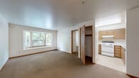 This 2-bedroom, 1-bathroom unit offers a practical and efficiently organized single-floor layout. The spacious primary bedroom is notably generous in size, featuring wall-to-wall carpeting, neutral white walls, and a large bay-style window that frames views of surrounding greenery, filling the room with natural light. The second bedroom is also carpeted and includes a sliding-door closet with built-in shelving and a window with blinds, making it a versatile space for sleeping or other uses.

The open living area connects seamlessly to the rest of the unit, with warm-toned wood door and trim accents contrasting the crisp white walls. Multiple doors lead to the bedrooms, a storage closet, and the kitchen, which features light wood cabinetry and white appliances including a range. The layout, as seen from the overhead dollhouse view, is compact yet well-partitioned, maximizing the use of available space.

The bathroom is clean and functional, equipped with a single-sink vanity with wood cabinetry, a full tub-shower combination with grab bars, and tile flooring in a neutral tone. Throughout the unit, consistent carpeting, smooth ceilings, and wood-trimmed doorways create a cohesive and straightforward aesthetic suited for everyday living.