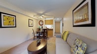 This single-floor residential unit offers a thoughtfully arranged layout that balances comfort and functionality across its key living spaces. The living room serves as the central gathering area, featuring plush carpeting, a neutral-toned sofa accented with chartreuse and patterned throw pillows, a round wooden coffee table, and framed wall art that contributes to a warm, cohesive aesthetic. A ceiling fan with integrated lighting adds both comfort and practicality to the space.

Adjacent to the living room, the dining area accommodates a round wooden table with four chairs, lit by a matching ceiling fan fixture overhead. Coordinating framed artwork lines the walls, maintaining the unit's consistent design language.

The galley-style kitchen is efficiently designed with white cabinetry lining both walls, offering ample storage. Wood-toned flooring, a white electric range, refrigerator, dishwasher, and a stainless steel sink provide all essential conveniences. Light countertops maximize the sense of brightness in the compact space.

The bedroom is carpeted and comfortably sized, featuring a window that allows natural light and a view of greenery outside. A sliding closet provides convenient storage, and a wall-mounted heater ensures year-round comfort.

The bathroom features wood-look flooring, a single-sink vanity with built-in cabinetry, a lighted mirror, and a clean, functional layout. Throughout, the unit maintains a warm neutral palette that creates an inviting and cohesive atmosphere.