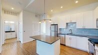 Located at 8995 E 47th Ave in Denver's Central Park neighborhood, this single-floor residence offers a well-designed layout with contemporary finishes throughout. The kitchen serves as the heart of the space, showcasing white shaker-style cabinetry, dark countertops, and a light blue subway tile backsplash. A central island with a dark countertop provides additional workspace and is illuminated by a trio of pendant lights suspended from the elevated ceiling. Stainless steel appliances, including a refrigerator, dishwasher, microwave, and range, complete the kitchen. Warm hardwood-style flooring flows throughout the main living and kitchen areas, adding cohesion to the open layout.

The bedroom offers generous proportions, soft carpet underfoot, and a closet with built-in rods for storage. Corner-facing windows flood the room with natural light and frame elevated views of the surrounding Denver skyline and neighborhood. The bathroom features a white vanity with a dark countertop, an undermount sink, chrome fixtures, and a large mirror with overhead lighting. The overall aesthetic of the space is clean, modern, and bright, with a neutral palette that creates a welcoming and functional environment.