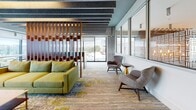 This thoughtfully designed single-floor commercial space seamlessly combines industrial aesthetics with contemporary style. The open lounge area is anchored by bold chartreuse sofas and mid-century modern accent chairs in warm grey tones, set atop a richly patterned carpet that weaves together greens, blues, and neutrals. Overhead, exposed concrete ceilings are accented by dark acoustic baffles and warm linear lighting, lending a sophisticated industrial character throughout.

A distinctive slatted wood partition screen divides zones while maintaining an open, airy flow between spaces. Interior glass walls with decorative frosted patterning offer visual interest and partial privacy to adjacent areas, including what appears to be a reception or service counter adorned with colorful artwork.

Floor-to-ceiling windows line the perimeter, flooding the space with abundant natural light and framing sweeping views of the surrounding landscape and cityscape. A bar-height countertop workstation runs along one window wall, paired with vibrant teal seating — an ideal setting for focused work or informal collaboration.

A lounge nook features a deep navy accent wall with a wall-mounted flat-screen display, complemented by yellow-green modular seating and teal ottomans, creating a lively media or breakout zone. Access to an outdoor terrace further extends the usable space, offering al fresco seating with open views.