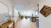 This well-appointed two-story home provides generous living space across two thoughtfully designed floors. The main level features an open-concept layout that seamlessly connects the living room, dining area, and kitchen, all unified by light hardwood flooring and abundant natural light from large windows. The kitchen stands out with slate-blue shaker cabinetry, a white quartz waterfall island with bar seating, subway tile backsplash, and stainless steel appliances. The adjacent living area includes sliding glass doors that open to the outdoors, enhancing the bright, connected feel of the space.

The upper level, which comprises the larger portion of the home, houses all three bedrooms, three full bathrooms, a dedicated office, and a conveniently located laundry room with a full-size washer and dryer. The primary bedroom includes a well-organized walk-in closet with built-in shelving and hanging rods. The bathrooms feature blue-gray vanities with white countertops. The office is a bright, functional room with a large window. Throughout, the home maintains a clean, modern palette of neutral tones, recessed lighting, and consistent hardwood flooring.