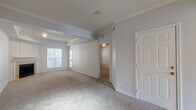 This single-floor residence offers a thoughtfully laid-out interior with a variety of functional and comfortable spaces. The spacious living room serves as the heart of the home, featuring a tray ceiling accented by crown molding and a tile-surround fireplace as its focal point. Natural light filters through a window overlooking an outdoor area, while neutral carpet and crisp white walls create a clean, welcoming atmosphere. An open passageway connects the living area to additional rooms, maintaining a sense of flow throughout.

The kitchen is outfitted with wood-toned cabinetry featuring white panel fronts, laminate countertops, and hardwood-style flooring. White appliances, including a coil-burner range, dishwasher, and refrigerator, are neatly integrated within a U-shaped layout that maximizes workspace efficiency. A window above the sink provides natural light.

The bedroom is generously sized, with two windows and a ceiling fan with light fixture. It benefits from an expansive closet system featuring dedicated shelving on one side and a hanging rod on the other, offering versatile storage options.

The bathroom includes hardwood-style flooring, a vanity with laminate countertop, and a full tub-shower combination with white tile accented by a warm terracotta border stripe.