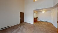 This two-story unit located in Portage, Indiana offers a functional and straightforward layout spread across two levels. The main level features a living area with striking vaulted ceilings that rise dramatically, creating an open and airy atmosphere. Carpeted flooring runs throughout the living spaces, adding warmth underfoot, while a wall-mounted air conditioning unit and baseboard heating provide year-round climate control. A staircase with a wooden railing connects the main level to the upper floor. Adjacent to the living area, the kitchen is equipped with warm oak cabinetry, dark laminate countertops, a white electric range, a refrigerator, and tile flooring. A drop ceiling with panel lighting gives the kitchen a defined, enclosed feel. A ceiling fan in the dining area provides additional air circulation.

The upper level features rooms with angled, vaulted ceilings that follow the roofline, enhancing the sense of height. Carpeted bedrooms receive natural light through horizontal blind-covered windows, and baseboard heaters line the walls. The bathrooms on both levels are consistently appointed with warm wood vanity cabinetry, mirrored medicine cabinets with globe or bar lighting, light countertops, and tile flooring, offering a cohesive and practical design throughout.