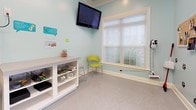 Pup Wash is a dedicated self-serve dog grooming facility located at 1341 Ellis Forest Rd in Kernersville, NC. The single-floor space is thoughtfully designed with pet owners and their dogs in mind, combining functionality with a cheerful, inviting atmosphere. The interior is finished with light aqua-blue walls accented by white subway tile wainscoting, giving the space a clean, fresh aesthetic. Durable speckled epoxy flooring runs throughout, ensuring easy maintenance and a polished look.

The main grooming area is the centerpiece of the facility, featuring a stainless steel professional dog wash tub equipped with a handheld sprayer, steps for easy pet access, and a wall-mounted high-velocity pet dryer — everything needed for a thorough wash. Grooming supplies and products are neatly organized on open shelving nearby. Playful paw print decals adorn the walls, reinforcing the space's pet-friendly character.

A separate area provides a comfortable waiting and preparation zone, complete with a wall-mounted flat-screen TV, a large window with blinds that allows natural light to fill the room, and seating for clients. A glass-paned French door connects the interior rooms, maintaining an open, airy feel. The facility's entrance features a windowed door with views to the exterior, a bulletin board with informational signage, and convenient storage for aprons and accessories.