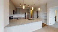 This single-floor residence is thoughtfully designed with a clean, contemporary aesthetic carried throughout each space. The kitchen serves as a central highlight, featuring grey shaker-style cabinetry, white subway tile backsplash, and granite countertops extending across both the perimeter surfaces and a generously sized island with an undermount sink. Pendant lighting illuminates the island, while a full suite of stainless steel appliances—including a refrigerator, range, microwave, and dishwasher—completes the space. Light hardwood-style flooring runs through the kitchen and connecting hallway, contributing to a bright, cohesive look.

The bedrooms are finished with plush carpeting and feature multiple windows with blinds that allow natural light to fill each room. Both walk-in closets are equipped with wire shelving systems, offering organized and practical storage. The primary bathroom includes a dual-sink vanity topped with granite, grey cabinetry with brushed nickel hardware, and large-format tile flooring. A separate tub and shower combination with white subway tile adds a classic finishing touch. The hallway connecting all areas is clean and well-lit, reinforcing the home's bright, neutral palette throughout.