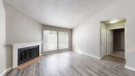 This single-story, 3-bedroom, 2-bathroom home offers a thoughtfully designed layout that maximizes functionality and comfort. The open-concept living room immediately impresses with soaring vaulted ceilings, a ceiling fan, and a classic wood-burning fireplace flanked by large windows that flood the space with natural light and offer views of surrounding greenery. Durable wood-style flooring runs throughout the main living areas, adding warmth and a cohesive aesthetic.

The kitchen is efficiently laid out in a galley style, featuring rich dark wood cabinetry, granite countertops, a tile backsplash, and black appliances including a refrigerator, range, and microwave. A pass-through counter connects the kitchen to the living area, enhancing the open feel.

The three bedrooms are carpeted for comfort, each offering neutral tones and ample space. The primary bedroom is generously sized, while the secondary bedrooms each include closets with bi-fold doors. The two bathrooms are clean and functional, with one featuring a full tub-and-shower combination with white tile surround and dark wood cabinetry. A dedicated laundry area and two hallways complete the practical layout, providing convenient storage and circulation throughout the home.