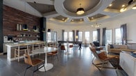 This contemporary community clubhouse in Plainfield, Indiana is thoughtfully designed to offer a variety of social and functional spaces across a single floor. The heart of the facility is a spacious open-plan lounge and recreation area anchored by a striking rotunda ceiling with layered tray detailing and elegant pendant lighting. Large windows dressed with dramatic floor-to-ceiling curtains flood the space with natural light and provide views of the outdoor patio area beyond. Large-format tile flooring flows throughout, lending a cohesive, upscale feel.

The lounge area features a prominent accent wall finished in a herringbone tile pattern, framing a linear fireplace and wall-mounted television beneath soaring ceilings and a statement chandelier. A dedicated game room includes a shuffleboard table and billiards, while a casual seating nook with sofas and accent chairs offers a relaxed retreat. The kitchen area showcases an exposed brick accent wall, open shelving, modern pendant lights, and an island with bar seating—ideal for social gatherings. Additional dining and banquet seating areas accommodate larger groups with built-in booth-style benches.

A private conference room with a round table and wall-mounted display provides a quiet workspace, while a bright co-working area features long desks, multiple workstations, and expansive windows with exterior views.