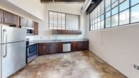 Located in downtown Winston-Salem, this 2-bedroom, 2-bathroom unit showcases an industrial-chic aesthetic throughout. Polished concrete floors, exposed metal ductwork, and steel beam accents define the character of the space. Large factory-style windows flood the living areas with natural light and offer urban street views. The kitchen features rich dark cabinetry, granite countertops, and a full suite of stainless steel appliances. Both bedrooms include built-in closets with wood-accented doors. The bathrooms are finished with granite-topped vanities, dark cabinetry, and tile flooring, maintaining a consistent design language across the entire unit.