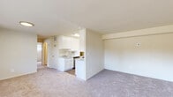This single-floor, 2-bedroom, 1-bathroom unit offers a practical and efficiently designed layout within a compact footprint. The living room serves as the central gathering space, featuring neutral carpet flooring, warm beige walls, and multiple windows that allow natural light to fill the room. A front entry door flanked by windows provides views of surrounding greenery, enhancing the bright, airy atmosphere.

The kitchen is positioned adjacent to the living area and is outfitted with white cabinetry, granite-style countertops, stainless steel appliances including a gas range, refrigerator, dishwasher, and microwave. A stackable in-unit washer and dryer are conveniently integrated into the kitchen space, adding practical value. Wood-look flooring grounds the kitchen area.

Both bedrooms are carpeted and bathed in natural light from sizable windows with blinds. The primary bedroom offers a generous closet with a built-in shelf and hanging rod. The second bedroom is comparably sized and similarly finished.

The bathroom features white square-tile walls surrounding a full soaking tub with shower, complemented by a white vanity with sink and wood-look flooring, maintaining a clean, cohesive aesthetic throughout.