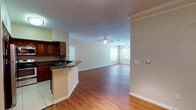 This single-floor residence is designed with an open-concept layout that connects the kitchen and living area into one cohesive, well-lit space. The living room features warm hardwood-style flooring, crown molding, and a ceiling fan, creating a comfortable and polished atmosphere. Natural light filters in through windows at the far end of the living area, adding brightness to the space.

The kitchen is positioned along one side of the open area, separated by a peninsula counter finished with dark granite countertops. Rich, dark-toned cabinetry extends to the upper walls, providing ample storage, while stainless steel appliances—including a refrigerator, electric range, and over-the-range microwave—complete the functional setup. Light tile flooring distinguishes the kitchen from the adjoining living space.

The bedrooms are carpeted and each include a ceiling fan and windows that allow natural light and outdoor views. Closet space is accessible from the bedroom areas. The bathrooms feature tile flooring and a tub-shower combination with white tile surround. A walk-in closet with wire shelving is accessible from one of the bathroom areas, adding practical storage. Overall, the unit maintains a neutral, warm palette throughout.