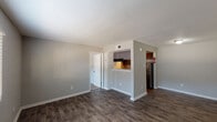 This single-story, one-bedroom, one-bathroom unit in Houston, TX (77090) offers a practical and well-appointed layout designed for comfortable living. The main living area is finished with rich, dark hardwood-style flooring and neutral gray walls, creating a clean, modern aesthetic throughout. A pass-through window with accent lighting connects the living space to the kitchen, providing an open feel between the two areas. The galley-style kitchen is efficiently designed, featuring dark cabinetry, light stone-patterned countertops, a stainless steel refrigerator, and an electric range, all beneath a textured ceiling with built-in ventilation. The bedroom is carpeted and includes a ceiling fan with a window dressed in blinds that allows natural light to filter in. A generously sized walk-in closet with wrap-around shelving and hanging rods provides ample storage. The bathroom includes a full tub-and-shower combination with tiled surround. White trim and baseboards run consistently throughout the unit, complementing the neutral color palette. The overall ambiance is clean, functional, and move-in ready, suited for single occupants or couples seeking a manageable, low-maintenance living space in Houston.