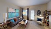 Located at 10300 20th St E in Edgewood, Washington, this single-floor residence offers a thoughtfully designed layout with contemporary finishes throughout. The kitchen is a standout feature, equipped with stainless steel appliances including a refrigerator, microwave, and range, complemented by rich dark cabinetry, granite countertops with a double-basin sink, and wood-look flooring that extends through the entryway and main areas. The open entry provides a clear sightline into the kitchen, enhancing the sense of flow. The living room offers carpeted flooring, natural light from a window with decorative curtains, and a sliding glass door that opens to an outdoor area. A dedicated dining nook features hardwood-style flooring, a pendant chandelier, and a mirrored wall accent. The bedroom is carpeted and well-lit by a window with blinds and patterned curtains. Two bathrooms serve the unit — one featuring a shower/tub combination with a full vanity and wood-look flooring, and the other a smaller half-bath style space with a dark wood vanity, mosaic tile backsplash, and open shelving. The overall aesthetic is modern and cohesive, with neutral tones and consistent dark wood accents throughout.