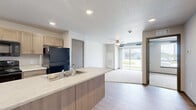 Located in Waukee, Iowa, this well-designed one-bedroom, one-bathroom unit offers a practical and comfortable single-floor layout. The open-concept kitchen serves as the heart of the space, showcasing light wood cabinetry, a large peninsula island with a double-basin sink and light countertops, and a full suite of black appliances including a range, microwave, and refrigerator. Light hardwood-style flooring runs throughout the main living and kitchen areas, contributing to a clean, modern aesthetic. Recessed lighting illuminates the kitchen, enhancing the bright and airy feel of the space. The bedroom is a cozy retreat finished with soft carpeting and featuring a generously sized window that brings in natural light and offers views of the surrounding neighborhood. The full bathroom is finished in crisp white tones, complete with a soaking tub and shower combination, a toilet, and hardwood-style flooring. A dedicated in-unit laundry room includes both a full-size washer and dryer along with open wire shelving for additional storage. The overall design emphasizes functionality and clean, contemporary finishes throughout, making this a practical and inviting home in the growing Waukee community.
