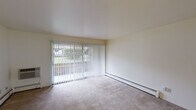 Located at 3115 S Westnedge Ave in Kalamazoo, Michigan, this single-floor unit offers a straightforward, functional layout with several notable features throughout. The living area is generously sized, finished with neutral-toned carpet and smooth white walls that create a clean, bright atmosphere. A full-width sliding glass door fitted with vertical blinds connects the living space to an outdoor area, allowing substantial natural light to fill the room. Baseboard heating units run along the exterior walls, providing efficient climate control throughout the space.

Additional rooms, visible in the floor plan overview, include what appears to be a separate bedroom area with a large picture window dressed in vertical blinds, also carpeted and equipped with baseboard heating. A secondary carpeted room features overhead lighting and open access to adjacent spaces, offering flexibility in use.

The kitchen is equipped with warm-toned wood cabinetry, granite-style countertops, a white electric range with an overhead ventilation hood, and tile flooring, providing a practical and organized cooking space. The bathroom includes a full tub and shower combination with white square tile surround, chrome fixtures, and a safety grab bar, reflecting a functional and accessible design throughout this Kalamazoo residence.
