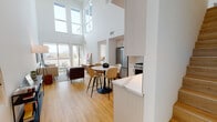 Located at 8809 Washington Blvd in Culver City, California, this contemporary two-story residence combines modern design with an abundance of natural light and impressive urban views. The open-concept living and dining area is anchored by dramatic double-height ceilings and expansive floor-to-ceiling windows that flood the space with sunlight, while sliding glass doors lead to a private outdoor terrace overlooking the cityscape. Light-toned hardwood flooring flows seamlessly throughout the main living areas, enhancing the bright, airy atmosphere. The kitchen is outfitted with white shaker cabinetry, white tile backsplash, quartz countertops, and a full suite of stainless steel appliances, including a gas range, built-in microwave, refrigerator, and dishwasher. The bedrooms are generously proportioned, each featuring large windows that frame panoramic views of the surrounding Culver City and Los Angeles skyline. The bathroom is finished with large-format tile flooring and elegant marble-veined wall tile surrounding a full soaking tub and shower combination with brushed gold fixtures. A cozy sitting area with direct access to an additional outdoor terrace adds versatile living space. Throughout, the residence maintains a clean, minimalist aesthetic defined by white walls, modern finishes, and thoughtful architectural detailing.