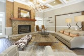 This single-floor space combines rustic charm with refined elegance throughout its thoughtfully designed interiors. The centerpiece of the main lounge area is a commanding floor-to-ceiling stacked stone fireplace, crowned with a rich wood mantel and a rustic-framed mirror. Warm hardwood floors flow throughout, complementing the textured cork accent wall that flanks the fireplace. An ornate chandelier with amber-toned crystals anchors the lounge, casting a warm glow over the seating area.

The entry foyer makes a strong first impression with its grand arched entryway featuring floor-to-ceiling glass-paned double doors, flanked by arched windows that flood the space with natural light and offer views of the lush greenery outside. Coffered ceilings with crown molding add architectural sophistication to this welcoming area.

A dedicated office or leasing area is framed by exposed natural wood beams, lending a warm, lodge-inspired aesthetic. This workspace includes a central desk, pendant lighting, and a service counter with transom windows, creating a functional yet stylish professional environment. A corridor leads to additional private rooms. Throughout the space, wainscoting, neutral wall tones, and carefully curated furnishings contribute to an inviting, upscale atmosphere.