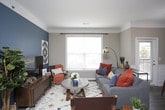 This thoughtfully designed single-floor residence offers a cohesive blend of comfort and style throughout its well-organized layout. The open-concept kitchen is a functional centerpiece, outfitted with warm wood cabinetry, granite countertops, black appliances, and a spacious island with a built-in sink and pendant lighting overhead. Durable wood-look flooring runs through the main living areas, adding warmth and continuity. Adjacent to the kitchen, the dining area features elegant wainscoting, a bold teal accent wall, a chandelier, and a large window that brings in natural light. The living room continues the teal accent wall theme and is generously lit by multiple windows, creating a bright, welcoming atmosphere with crown molding adding a refined touch. The bedrooms are carpeted for comfort, each equipped with a ceiling fan. One bedroom showcases a vibrant orange accent wall and a walk-in closet with built-in hanging storage. A second bedroom offers a window with sheer curtains and a dresser nook. The bathroom is finished with granite countertops, a tub-shower combination with sliding glass doors, and tasteful framed wall art. Overall, the residence presents a cohesive, well-maintained interior with consistent design details throughout.