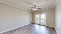 This one-bedroom, one-bathroom unit at The Lynx in Webster, Texas offers a well-designed single-floor layout with a clean, modern aesthetic throughout. The living area features stylish wood-look plank flooring, crown molding, and a ceiling fan with light kit. French doors lead to a private balcony, filling the space with natural light and providing a seamless indoor-outdoor connection. The kitchen is thoughtfully appointed with white upper cabinetry, gray lower cabinets, white quartz countertops, a subway tile backsplash, and a full suite of stainless steel appliances including a refrigerator, range, and microwave. A peninsula with an undermount sink and pendant lighting adds both function and style, while light tile flooring ties the space together. The bedroom is carpeted for comfort and features multiple windows that invite natural light, along with a ceiling fan. A generously sized walk-in closet with wire shelving provides ample storage. The bathroom includes gray cabinetry with a white countertop vanity, tile flooring, and a tub/shower combination. The entryway features crown molding and tile flooring, creating a polished first impression upon entry.