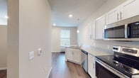 Located in DeForest, WI, this thoughtfully designed single-floor unit offers a clean, modern aesthetic with an open and functional layout. The kitchen serves as the centerpiece of the space, showcasing white shaker-style cabinetry, granite countertops, a peninsula with an undermount sink, and a full suite of stainless steel appliances including an electric range, dishwasher, and microwave. Elegant pendant lighting accents the peninsula, while recessed ceiling lights provide bright, even illumination throughout. Rich hardwood-style flooring flows seamlessly across the main living areas, complementing the neutral warm-gray wall tones and crisp white trim. The open living area adjacent to the kitchen offers a generous, versatile footprint, with a ceiling fan adding both functionality and comfort. A hallway with a Shaker-style closet door connects to the private areas of the unit, including a well-appointed bathroom featuring a granite-topped vanity with white cabinetry, a large mirror, and coordinating hardwood-style flooring. Natural light filters in through window treatments, enhancing the bright and airy feel of the space. The overall ambiance is fresh, contemporary, and move-in ready.