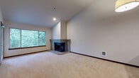 This single-floor residence offers a thoughtfully arranged layout with a variety of distinctive architectural and design elements. The entryway welcomes residents with rich hardwood-style flooring and dark-trimmed doors, establishing a warm, consistent aesthetic carried throughout the home.

The living room serves as a central highlight, featuring soaring vaulted ceilings that enhance the sense of openness, soft neutral carpeting, and a corner brick fireplace that adds a classic, cozy focal point. A large window frames views of lush surrounding greenery, filling the space with natural light.

Adjacent to the living room, the kitchen is well-appointed with dark espresso cabinetry, light granite countertops, stainless steel appliances including a range, microwave, and dishwasher, and hardwood-style flooring. A breakfast bar provides an open connection to the living area.

The hallway leads to additional carpeted rooms, including a generously sized bedroom with neutral tones and ample wall space. The bathroom is well-equipped, featuring both a soaking tub with tile surround and a separate glass-enclosed shower, complemented by a dark vanity with a wide countertop and hardwood-style flooring. An in-unit laundry area is conveniently accessible nearby.