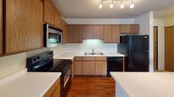 Located at 10761 Smetana Rd in Minnetonka, Minnesota, this single-floor residence offers a well-organized layout with distinct living, kitchen, and sleeping areas. The kitchen serves as a functional centerpiece, featuring warm wood cabinetry extending to the ceiling, white countertops, and a full suite of black appliances including a refrigerator, electric range, built-in microwave, and dishwasher. Track lighting illuminates the space, and a peninsula with a breakfast bar provides additional prep and seating space. Rich hardwood-style flooring runs throughout the kitchen and connects to adjacent hallways.

The living area is generously sized, finished with neutral carpet and a textured ceiling. A distinctive curved bay window arrangement floods the room with natural light and provides views of the surrounding greenery, while baseboard heating lines the perimeter. A ceiling fan adds to the comfort of the space.

The bedroom offers comfortable proportions, also carpeted, with access to a spacious walk-in closet with built-in shelving. A full bathroom is accessible from the hallway, featuring a tub-shower combination, toilet, and hardwood-style flooring, complemented by a closet for additional storage. The overall aesthetic is neutral and functional throughout.
