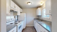 Located at 1248 Cedar Ave in Marysville, WA, Unit 13 is a single-floor residence offering a clean, functional layout with a bright and neutral aesthetic throughout. The entryway opens into a generously sized living area finished with durable wood-look plank flooring, crisp white walls, and a ceiling fan with light fixture. A sliding glass door floods the space with natural light and provides direct access to a private patio overlooking a grassy yard. A baseboard heating system and additional window ensure comfort and ventilation year-round. The galley-style kitchen is well-appointed with white cabinetry featuring brushed nickel hardware, gray laminate countertops, a double-basin sink, and white appliances including an electric range and full-size refrigerator. Overhead lighting and a window contribute to a bright workspace. The bedrooms are carpeted for comfort and offer ample space, with neutral wall tones and standard closet access. The bathroom includes a single vanity with a stone-look countertop, an undermount sink, and wood-look tile flooring. A textured ceiling is consistent throughout the common areas, lending a classic residential character to the overall space.