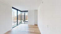 This well-appointed one-bedroom, one-bathroom residence combines modern design with functional living across a single floor. Light hardwood flooring flows consistently throughout the space, creating a cohesive and airy aesthetic.

The open-plan kitchen and living area form the heart of the home. The kitchen is thoughtfully designed with warm wood cabinetry extending to the ceiling, a textured tile backsplash, stone countertops, and a full suite of stainless steel appliances including a refrigerator, dishwasher, range, and microwave. The adjacent living area benefits from dramatic floor-to-ceiling corner windows framed in sleek black, flooding the space with natural light and offering expansive urban skyline views.

The bedroom continues the clean, minimalist aesthetic with the same hardwood flooring and its own set of large floor-to-ceiling windows showcasing city views. A closet and access to the hallway complete the room's practical layout.

The hallway connects the main living areas to the bedroom and bathroom, and features a louvered closet door adding a subtle architectural detail. The bathroom is finished with large-format neutral tiles surrounding a soaking tub and shower combination, complemented by modern brushed metal fixtures and a wood-toned vanity. The overall ambiance is clean, contemporary, and light-filled.