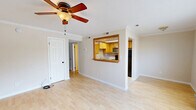 Located at 1212 West Ocean View Avenue in Norfolk, Virginia, this two-bedroom, one-bathroom residence offers a practical and well-organized single-floor layout. The living room serves as the heart of the home, featuring light hardwood flooring, crown molding, a ceiling fan with light fixture, and a window that invites natural light. A distinctive pass-through window connects the living area to the kitchen, which is outfitted with warm honey-toned cabinetry, a built-in microwave, and standard appliances including a refrigerator — creating an open, connected feel between the two spaces. Both bedrooms are carpeted for comfort and each includes a ceiling fan and a built-in bi-fold closet for storage. Natural light filters in through windows fitted with horizontal blinds. The full bathroom features tile flooring, a tub-shower combination, and clean white fixtures. A hallway connects the main living areas to the bedrooms and bathroom, maintaining a logical and efficient flow throughout the home. Neutral wall tones throughout create a clean, move-in-ready aesthetic suitable for a variety of furnishing styles.