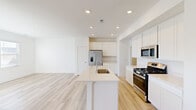 This well-designed two-story home offers a clean, contemporary aesthetic defined by a neutral palette of crisp whites and light tones throughout. The main level centers around an open-concept kitchen and living area, where light hardwood-style flooring flows seamlessly underfoot. The kitchen is thoughtfully equipped with white cabinetry reaching to the ceiling, stainless steel appliances including a gas range, built-in microwave, and French door refrigerator, all anchored by a generous island featuring a single-basin sink and light quartz countertops. Recessed lighting illuminates the space efficiently. Sliding glass doors and multiple windows on the main floor invite an abundance of natural light into the open living area. Upstairs, the bedrooms are carpeted for comfort and feature large windows offering neighborhood views. One bedroom benefits from vaulted ceilings and rich natural light. A spacious walk-in closet with wire shelving provides ample storage. The primary bathroom presents a dual-sink vanity with quartz countertops, a separate walk-in shower, and tile flooring, while a secondary bathroom offers a full tub-shower combo. Throughout both levels, the home maintains a fresh, move-in-ready feel with consistent finishes and thoughtful layout.