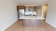 This contemporary 3-bedroom, 3-bathroom townhome spans two floors and 1,540 square feet of thoughtfully designed living space. The ground floor houses an attached garage with a Chamberlain opener and concrete flooring, along with an electrical panel and interior access door. The main living floor features an open-concept kitchen and living room area with light hardwood-style flooring, recessed lighting, and abundant natural light from multiple windows and a sliding glass door leading to a private balcony with views of the surrounding community. The modern kitchen is anchored by a large center island with a white quartz countertop and sink, complemented by rich wood-toned cabinetry, stainless steel appliances including a refrigerator, range, and built-in microwave, and a classic white tile backsplash. The three bedrooms are carpeted and well-sized, with the primary bedroom spanning 290 square feet. Each bedroom includes a closet. The three bathrooms are finished with wood-tone vanities and white quartz countertops; the primary bath features a dual-sink vanity with a large mirror, modern light fixtures, and a separate walk-in shower. Each floor is connected by staircases, making for efficient circulation throughout this well-appointed townhome.