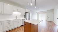 This single-floor, 2-bedroom, 2-bathroom residence offers a clean, modern design with a thoughtful layout. The open-concept kitchen and living area serves as the heart of the home, anchored by a striking center island with a quartz-style countertop and warm wood-toned base, complemented by pendant lighting overhead. White shaker-style cabinetry lines the walls alongside a white subway tile backsplash, and stainless steel appliances — including a refrigerator, range, microwave, and dishwasher — complete the kitchen. Warm-toned hardwood-style flooring flows throughout the main living area, which benefits from abundant natural light through a large sliding glass door fitted with vertical blinds. Both bedrooms are carpeted and feature windows with views of surrounding greenery, providing a calm, private retreat. Each bedroom is served by its own closet. The two bathrooms are finished with white cabinetry, quartz countertops, and hardwood-style flooring; one features a shower-tub combo, while the other offers a walk-in shower. Neutral wall tones and recessed lighting throughout the space contribute to a bright, cohesive aesthetic well-suited for comfortable everyday living.