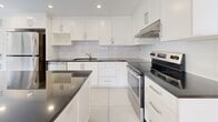 Located at 3470 Rue Stanley in the heart of Montréal, this expansive two-floor residence offers four bedrooms, four bathrooms, and a thoughtfully designed layout across two well-proportioned floors. The main floor provides an generous living footprint, while the upper level adds additional bedroom and living space, making this an ideal home for large households or those seeking room to spread out.

The modern kitchen is a standout feature, boasting white shaker-style cabinetry, dark granite countertops, a large central island, subway tile backsplash, and stainless steel appliances — all set on large-format white tile flooring. Multiple living rooms offer flexibility for entertaining or relaxing, each finished with warm parquet wood flooring in a classic basket-weave pattern. Large dark-framed windows span the living areas, allowing abundant natural light and framing views of the surrounding greenery and Montréal streetscape.

The four bathrooms are finished in crisp white tile, featuring glass-enclosed walk-in showers with mosaic tile floors and sleek chrome fixtures. The primary bedroom is a comfortable retreat with large windows. A dedicated laundry room with stacked washer and dryer adds everyday convenience. Hallways and a closet round out the practical layout of this well-appointed Montréal residence.