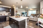 This single-floor residence offers a well-designed open-concept layout that seamlessly connects the kitchen, dining, and living areas. The kitchen is a standout feature, showcasing dark shaker-style cabinetry that reaches toward the ceiling, light quartz countertops, and a full suite of stainless steel appliances including a refrigerator, range, microwave, and dishwasher. A central island with pendant lighting above provides additional prep space and a casual gathering spot. Wood-look flooring runs throughout the main living areas, adding warmth and visual continuity.

The living room is generously sized, anchored by a large sliding glass door that opens to a private balcony, filling the space with natural light and outdoor views. The unit includes multiple bedrooms, each carpeted for comfort. One bedroom features a window with outdoor views, while another includes a spacious double-door closet. The bathroom is finished with wood-look flooring, a shower-tub combination, and a clean, neutral palette. Throughout the unit, a consistent neutral color scheme and textured ceilings contribute to a cohesive, move-in-ready ambiance.