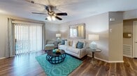 Located at Kessler Court in Garden City, Georgia, this single-floor residence offers a thoughtfully designed layout with multiple bedrooms and a cohesive, neutral color palette throughout. The living room serves as a comfortable central gathering space, featuring rich wood-look flooring, a ceiling fan with light fixture, and a sliding glass door that allows natural light to flow in and provides outdoor access. The kitchen is equipped with white shaker-style cabinetry, granite-look countertops, a double stainless steel sink, and a pass-through that connects to the adjacent living area. A dedicated dining area with hardwood-style flooring and wainscoting provides an ideal space for meals and entertaining. Each bedroom is carpeted for comfort and includes a ceiling fan, walk-in closet with built-in shelving, and windows dressed with blinds and coordinating curtains. The bathrooms feature white vanities with granite-look countertops, large mirrors, and a shower-tub combination with wood-look tile flooring. A dedicated laundry area houses a full-size side-by-side washer and dryer beneath overhead shelving, adding everyday convenience. The overall ambiance is warm and inviting, with consistent finishes tying each space together seamlessly.