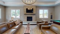 Located at 4214 California Rd in Orchard Park, NY, this single-floor community clubhouse is thoughtfully designed to offer residents an upscale, amenity-rich gathering space. The entrance lobby makes an immediate impression with its herringbone-patterned tile flooring, tray ceiling, and a striking gold sputnik chandelier. A display wall showcases available floor plans on acrylic panels above a live-edge wood bench, providing a welcoming orientation area for prospective residents.

The expansive lounge features rich dark hardwood flooring, warm neutral walls, and a floor-to-ceiling light brick fireplace framed by symmetrical windows that invite natural light and outdoor views. A circular candle-style chandelier crowns the seating area, which opens to a pass-through window with granite detailing that connects to the kitchen. The kitchen is fully equipped with stainless steel appliances, a gas range, a bold herringbone tile backsplash, dark cabinetry with granite countertops, and a spacious island with seating for multiple guests. A billiards table adds a recreational focal point to the open gathering area.

The dedicated fitness room is bright and energetic, outfitted with cardio equipment, rubber flooring, mirrored walls, and an accent wall bearing the motivational phrase "It's a Lifestyle." Recessed lighting and large windows complete this well-appointed space.