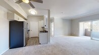 This single-floor, 2-bedroom, 1-bathroom unit offers a functional and comfortable layout with modern finishes throughout. The open-concept kitchen and living area serves as the heart of the home, featuring wood-look flooring, white cabinetry with sleek hardware, dark countertops, and a full suite of stainless steel appliances including a refrigerator, range, microwave, and dishwasher. A structural pillar subtly defines the boundary between the kitchen and the carpeted living area, which is topped with crown molding and a ceiling fan for added comfort. The primary bedroom is a generously sized retreat with plush carpeting, crown molding, and sliding glass doors that open onto a private balcony with outdoor views of surrounding greenery. The second bedroom also features carpet flooring, a ceiling fan, and multiple windows that bring in abundant natural light. The full bathroom is thoughtfully designed with a white vanity, dark countertop, wood-look flooring, and a glass-door tub-shower combination. Additional features include a dedicated laundry area with louvered bifold doors and a closet for extra storage. Soft, neutral gray tones used throughout the unit create a cohesive and calming aesthetic.