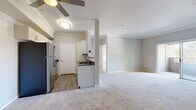 This single-floor, 2-bedroom, 1-bathroom unit offers a functional and comfortable layout with modern finishes throughout. The open-concept kitchen and living area serves as the heart of the home, featuring wood-look flooring, white cabinetry with sleek hardware, dark countertops, and a full suite of stainless steel appliances including a refrigerator, range, microwave, and dishwasher. A structural pillar subtly defines the boundary between the kitchen and the carpeted living area, which is topped with crown molding and a ceiling fan for added comfort. The primary bedroom is a generously sized retreat with plush carpeting, crown molding, and sliding glass doors that open onto a private balcony with outdoor views of surrounding greenery. The second bedroom also features carpet flooring, a ceiling fan, and multiple windows that bring in abundant natural light. The full bathroom is thoughtfully designed with a white vanity, dark countertop, wood-look flooring, and a glass-door tub-shower combination. Additional features include a dedicated laundry area with louvered bifold doors and a closet for extra storage. Soft, neutral gray tones used throughout the unit create a cohesive and calming aesthetic.