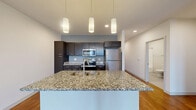 This contemporary 1-bedroom, 1-bathroom apartment in Madison, Wisconsin offers 1,000 square feet of thoughtfully designed living space. The open floor plan seamlessly integrates the kitchen, living, and dining areas, creating a spacious and airy atmosphere. The kitchen is a standout feature, boasting dark wood cabinetry, stainless steel appliances, and a striking granite countertop with a breakfast bar.

Large windows throughout flood the space with natural light, while providing scenic city views. The living area is expansive, with gleaming hardwood floors that extend into the bedroom. The bedroom, measuring 220 square feet, offers ample space and includes a ceiling fan for added comfort. A walk-in closet provides generous storage.

The bathroom features a modern design with a white tub/shower combination and clean lines. Additional amenities include recessed lighting, stylish pendant lights in the kitchen, and a full-sized washer and dryer. The apartment's neutral color palette and contemporary finishes create a sophisticated urban oasis, perfect for those seeking a blend of style and functionality in the heart of Madison.