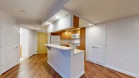This thoughtfully designed one-bedroom, one-bathroom unit offers a functional and cohesive single-floor layout. The open-concept kitchen and living area serves as the heart of the space, featuring warm hardwood flooring throughout and recessed lighting that keeps the area bright and inviting. The kitchen is well-equipped with honey-toned wood cabinetry, a full suite of white appliances including a refrigerator, electric range, and built-in microwave, and a white peninsula with an extended countertop that provides additional prep space and casual seating. The living area flows naturally from the kitchen and includes sliding glass doors that open to a private balcony, offering an outdoor retreat with views of the surrounding brick exterior. The bedroom is generously sized, finished with soft wall-to-wall carpeting, and includes dual closet doors providing ample storage. A separate dedicated closet further enhances storage options. The bathroom features a full-sized soaking tub and shower combination, accented by tasteful tan tile detailing near the ceiling. Neutral tones, clean white trim, and consistent finishes throughout create a cohesive and move-in-ready atmosphere.