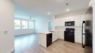 This single-floor unit offers a clean, contemporary design with a cohesive aesthetic carried throughout every room. The open-concept layout connects the kitchen and living area seamlessly, creating a spacious and functional shared space. The kitchen is well-appointed with crisp white cabinetry extending to the ceiling, a full suite of black appliances including a refrigerator, range, microwave, and dishwasher, and a peninsula with an integrated sink that doubles as a casual dining or prep area. Light wood-look flooring runs continuously through the kitchen and into the open living area, which benefits from a ceiling fan and large windows that invite generous natural light.

Multiple bedrooms are present, each featuring the same wood-look flooring, neutral warm-toned walls, a ceiling fan with light fixture, and windows with blinds that provide views of the surrounding neighborhood. The rooms offer a clean, versatile canvas well-suited for a variety of furniture arrangements.

The bathrooms maintain the unit's consistent modern palette, featuring white cabinetry with stone-look countertops, wood-look tile flooring, and a tiled shower-tub combination with chrome fixtures. Every space reflects a thoughtful, move-in-ready finish with a bright and airy ambiance throughout.