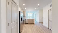 This single-floor unit offers a contemporary, open-concept layout that seamlessly connects the kitchen and living areas. The kitchen is a standout feature, equipped with stainless steel appliances including a French door refrigerator, range, microwave, and dishwasher. Light wood-tone cabinetry pairs with a classic subway tile backsplash and granite countertops, creating a clean, modern aesthetic. A peninsula with pendant lighting defines the kitchen space while keeping sightlines open to the living area. A built-in nook with a granite countertop and shelving provides a practical workspace or breakfast area just off the kitchen. Light wood-style plank flooring runs throughout the main living spaces, contributing to the bright, airy feel enhanced by recessed lighting throughout. The bedroom is carpeted for comfort and features dual windows that invite natural light and outdoor views, complemented by a ceiling fan. The bathroom is well-appointed with a soaking tub and tub-surround featuring large-format marble-style tile, a granite-topped vanity with wood-toned cabinetry, and wood-style flooring. Overall, the unit presents a cohesive, neutral palette with modern finishes throughout.