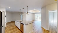 Located at Perkins Farm D in Mystic, Connecticut, this well-appointed 2-bedroom, 2-bathroom residence offers a thoughtfully designed open-concept layout with consistent, modern finishes throughout. Light hardwood flooring flows seamlessly across the entire space, complementing the bright, neutral palette that maximizes natural light.

The kitchen serves as a central hub, featuring a large granite-topped island with a built-in sink, pendant lighting, white shaker cabinetry, stainless steel appliances, and a distinctive teal subway tile backsplash. The kitchen opens directly into the living area, which benefits from a tray ceiling detail and sliding glass doors leading to a private balcony with views of the surrounding community.

The spacious primary bedroom includes a wall-mounted mini-split system and ample closet access, while the second bedroom also features a sliding glass door to an outdoor balcony, filling the room with natural light. Both bedrooms are generously proportioned and finished with the same warm hardwood flooring.

The two bathrooms maintain a clean, modern aesthetic with white shaker vanities, granite countertops, large mirrors, and white subway tile. The primary bath includes a walk-in glass shower, while the second bath offers a full soaking tub and shower combination. Every detail reflects a commitment to quality and contemporary design.
