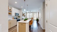 This thoughtfully designed single-floor residence offers a seamless blend of modern aesthetics and functional living. The open-concept layout connects the kitchen directly to the living and dining areas, creating a cohesive and airy flow throughout the space. Wide-plank wood-look flooring runs throughout the main areas, anchoring the light, neutral color palette.

The kitchen is a standout feature, equipped with stainless steel appliances including a refrigerator, range, microwave, and dishwasher. Two-tone cabinetry pairs white upper cabinets with natural wood lower cabinets, complemented by white quartz countertops and a subway tile backsplash. A central island with bar seating and pendant lighting serves as both a prep space and casual dining area.

The living room is bright and welcoming, with large windows and a glass door that invite abundant natural light and outdoor views. A ceiling fan adds to the comfort of the space.

The bedroom is a serene retreat with large windows, a walk-in closet, and direct access to an outdoor balcony. The bathroom features a wide vanity with quartz countertops, wood-tone cabinetry, a large mirror, and a shower-tub combination, maintaining the clean, contemporary style found throughout the residence.