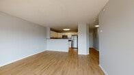 This single-floor unit offers a thoughtfully designed open-concept layout that seamlessly connects the living area and kitchen. The living space features warm, light-toned hardwood-style flooring and neutral gray walls, creating a clean and versatile atmosphere. A corner arrangement of large windows, paired with a door providing outdoor access, floods the space with natural light and offers pleasant views of surrounding greenery.

The kitchen is well-equipped with white shaker-style cabinetry providing ample storage, dark granite countertops, and a full suite of stainless steel appliances including a refrigerator, electric range, built-in microwave, and dishwasher. A peninsula-style breakfast bar separates the kitchen from the living area, adding both functionality and visual definition to the open floor plan.

The bedroom is finished with plush wall-to-wall carpeting, neutral tones, and a window that brings in natural light. The bathroom features a white vanity with undermount sink, granite-style countertop, and brushed gold hardware. Notably, an in-unit stacked washer and dryer is conveniently accessible from the bathroom area, adding a practical amenity to the overall layout.