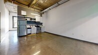 Located in the heart of Downtown Los Angeles on South Broadway, this one-bedroom, two-bathroom loft showcases an industrial-modern aesthetic throughout. Polished concrete floors run seamlessly across the entire space, reflecting light and reinforcing the unit's urban character. The open-concept living and kitchen area features soaring exposed concrete ceilings with visible wooden beams and ductwork, lending an authentic loft feel. The kitchen is outfitted with stainless steel appliances — including a refrigerator, electric range, dishwasher, and microwave — set against a navy blue accent wall with white cabinetry and a clean countertop with an undermount sink. The bedroom offers tall windows with black-framed casements that frame views of the surrounding Downtown skyline, filling the room with natural light. A sliding-door closet provides built-in storage. The bathroom features floor-to-ceiling subway tile surrounding a full soaking tub with an overhead shower, complemented by polished concrete floors consistent with the rest of the unit. The second bathroom adds additional convenience. The overall ambiance is clean, minimal, and distinctly urban — ideal for those seeking a contemporary loft experience in one of Los Angeles's most vibrant and walkable neighborhoods.