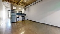 Located in the heart of Downtown Los Angeles on South Broadway, this one-bedroom, two-bathroom loft showcases an industrial-modern aesthetic throughout. Polished concrete floors run seamlessly across the entire space, reflecting light and reinforcing the unit's urban character. The open-concept living and kitchen area features soaring exposed concrete ceilings with visible wooden beams and ductwork, lending an authentic loft feel. The kitchen is outfitted with stainless steel appliances — including a refrigerator, electric range, dishwasher, and microwave — set against a navy blue accent wall with white cabinetry and a clean countertop with an undermount sink. The bedroom offers tall windows with black-framed casements that frame views of the surrounding Downtown skyline, filling the room with natural light. A sliding-door closet provides built-in storage. The bathroom features floor-to-ceiling subway tile surrounding a full soaking tub with an overhead shower, complemented by polished concrete floors consistent with the rest of the unit. The second bathroom adds additional convenience. The overall ambiance is clean, minimal, and distinctly urban — ideal for those seeking a contemporary loft experience in one of Los Angeles's most vibrant and walkable neighborhoods.