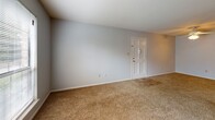 This single-story residence in Summerville, South Carolina offers a practical and straightforward layout across several interconnected spaces. The floor plan, visible in the overhead scan, reveals a well-organized arrangement of living, kitchen, and bedroom areas designed for comfortable everyday use.

The living area is generously sized, finished with wall-to-wall carpeting in a neutral tan tone and painted in a soft gray palette. A ceiling fan with integrated lighting provides both airflow and illumination. A paneled entry door with a tiled threshold marks the main access point to the space.

The kitchen is a functional U-shaped layout featuring rich, warm-toned wood cabinetry that extends to the upper walls, providing ample storage. Countertops with a speckled finish complement the cabinetry, while white appliances — including a coil-burner electric range, dishwasher, and full-size refrigerator — complete the setup. The flooring transitions to a stone-look vinyl tile, adding durability in this high-traffic area.

The bedroom spaces continue the carpeted flooring and neutral gray wall tones. One bedroom includes a ceiling fan with a window allowing natural light, while another features a bifold closet door for built-in storage.

The bathroom is clean and efficiently designed, with white subway tile surrounding a full tub-and-shower combination, a toilet, and a vanity. Wood-look tile flooring and chrome hardware finish the space with understated practicality.