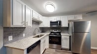 This single-floor unit presents a clean, updated aesthetic throughout its living spaces. The kitchen serves as a standout feature, showcasing white shaker-style cabinetry paired with granite countertops featuring subtle speckled detailing. A gray subway tile backsplash adds a contemporary touch, while a full suite of stainless steel appliances—including a refrigerator, electric range, over-the-range microwave, and dishwasher—provides a cohesive, modern look. Wood-look plank flooring runs through the kitchen and extends into the open living area, lending warmth and continuity across the space.

The living area is open and well-proportioned, finished with neutral gray walls, white baseboards, and a ceiling fan with light fixture. A wall-mounted air conditioning unit and a window with blinds provide both natural light and climate control. The bedroom features neutral carpet, gray walls, a ceiling fan, and a baseboard heater, creating a comfortable and functional space.

The bathroom is finished with wood-look flooring and includes a full tub-shower combination with white tile surround, a toilet, and a vanity with white cabinetry. Overall, the unit reflects a refreshed, move-in-ready interior with consistent, neutral finishes throughout.