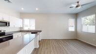 This single-story home presents a clean, modern aesthetic defined by neutral warm-beige walls, light wood-look vinyl flooring, and crisp white trim that flows consistently throughout. The open-concept kitchen and living area form the heart of the home, creating a cohesive, functional space filled with natural light from multiple windows dressed with white horizontal blinds.

The kitchen is a standout feature, showcasing white shaker-style cabinetry extending to the ceiling for ample storage, paired with dark quartz-style countertops that provide a sharp contrast. A central island offers additional prep space and casual seating potential. Stainless steel appliances — including a refrigerator, electric range, built-in microwave, and dishwasher — complete the modern setup. A undermount sink with a brushed nickel faucet sits beneath a window, enhancing the workspace with natural light.

The living area extends naturally from the kitchen, offering an open, versatile space with recessed lighting overhead and multiple windows bringing in abundant daylight. The bedroom features corner windows that maximize light and provide outdoor views. The bathroom is well-appointed with a glass-enclosed walk-in shower featuring white subway tile surround, built-in shelving niches, and a modern vanity with matching countertops.