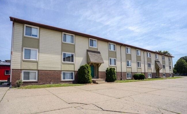 A three-story apartment building with grassy area, and clear blue sky. - Highland Apartments